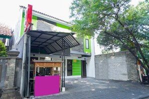 Un edificio con fachada verde y blanca, una entrada visible y un árbol al fondo.