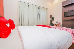 Habitación de hotel con una cama grande, un escritorio con silla, televisión en la pared y ventana con cortinas.