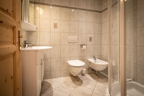 A bathroom with a toilet, bidet, sink, and shower.