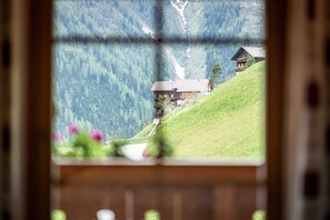 A mountain cabin with a view of a valley, a wooden deck, and a window with a view of the mountains. - Apartment Kreuzspitze on the second floor at House Gutwenger (Innervillgraten)