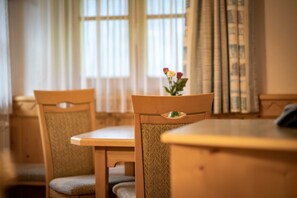 A dining area with a wooden table and chairs, a vase with flowers, and a window with curtains. - Apartment Kreuzspitze on the second floor at House Gutwenger (Innervillgraten)