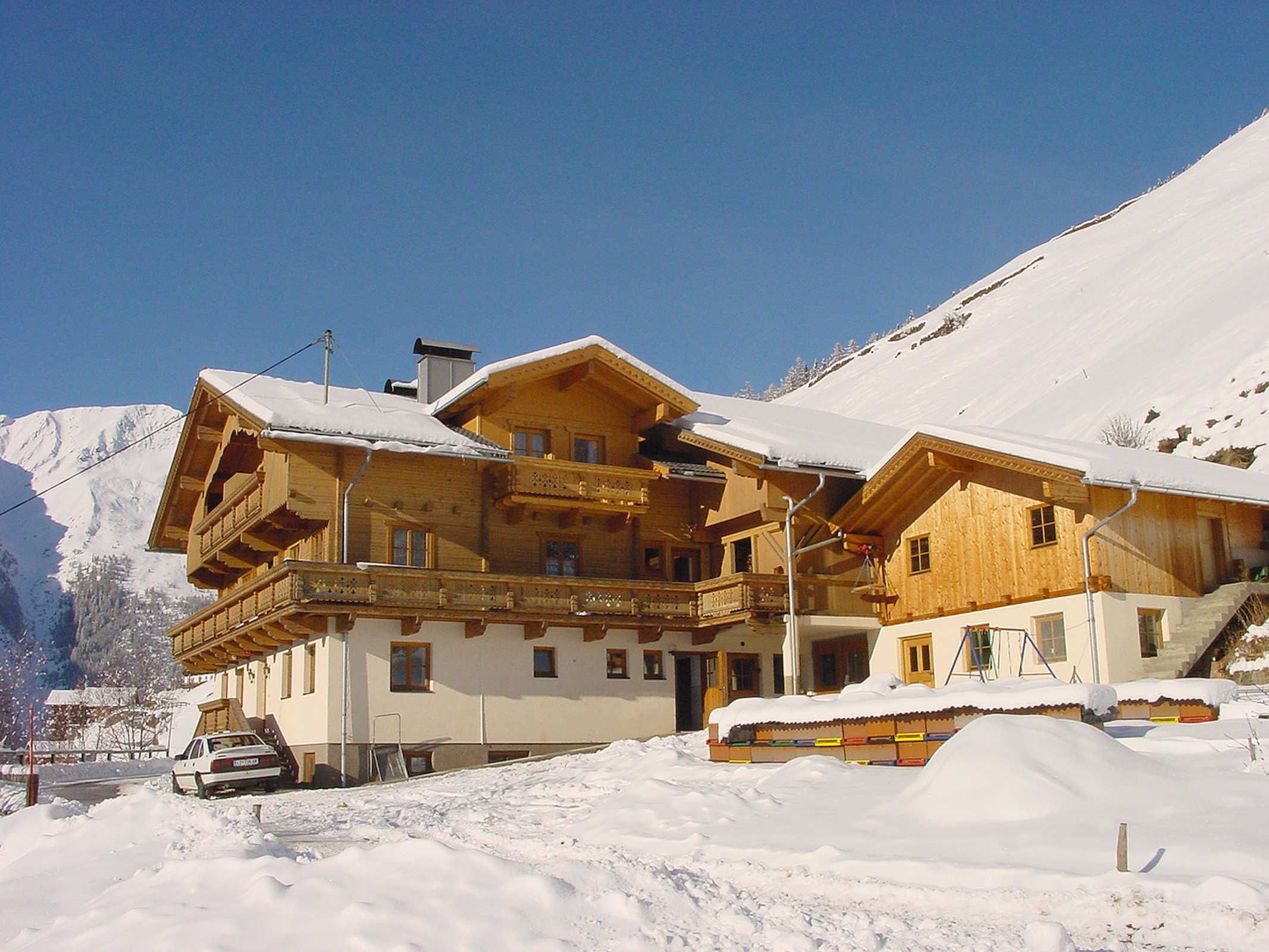 A wooden chalet with balconies, a car parked in front, and snow-covered surroundings.