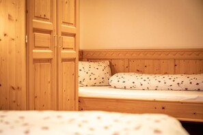A wooden bed with floral bedding, a wooden wardrobe, and a plain wall.