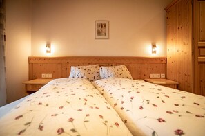 Un lit double avec une literie à motifs floraux, une tête de lit en bois, des tables de chevet et des lampes fixées au mur.