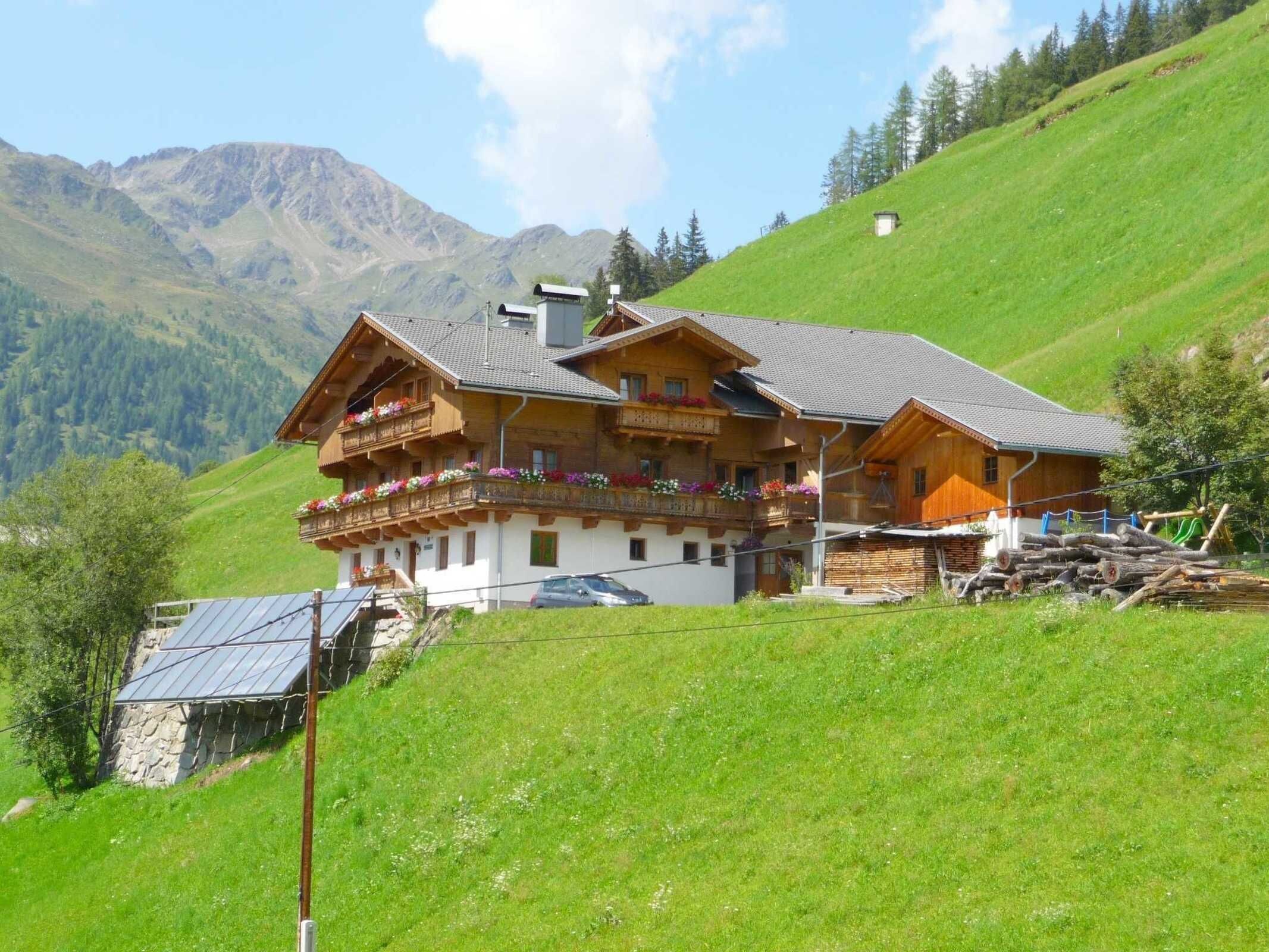 A chalet with a balcony, a stone wall, and a mountain backdrop.