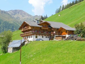 A chalet with a balcony, a stone wall, and a mountain backdrop. - Apartment Dorfblick - Apartmenthaus Gutwenger - Selmerhof (Innervillgraten)
