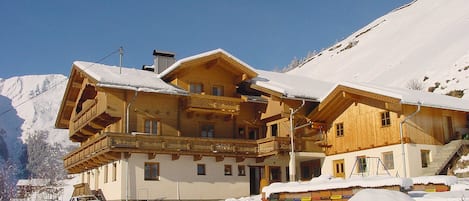 A wooden chalet with balconies, a car parked in front, and snow-covered surroundings.