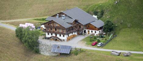A large, two-story wooden house with a sloped roof, a stone foundation, and a solar panel array.