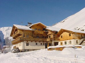 A wooden chalet with balconies, a car parked in front, and snow-covered surroundings. - Apartment Hochberg at House Gutwenger (Innervillgraten)