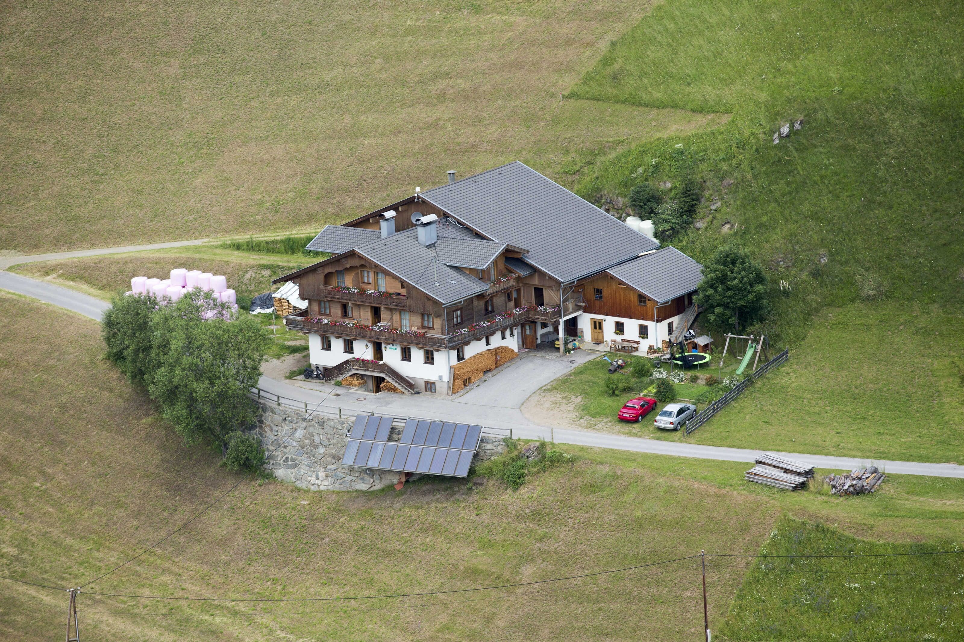 A large, two-story wooden house with a sloped roof, a stone foundation, and a solar panel array.