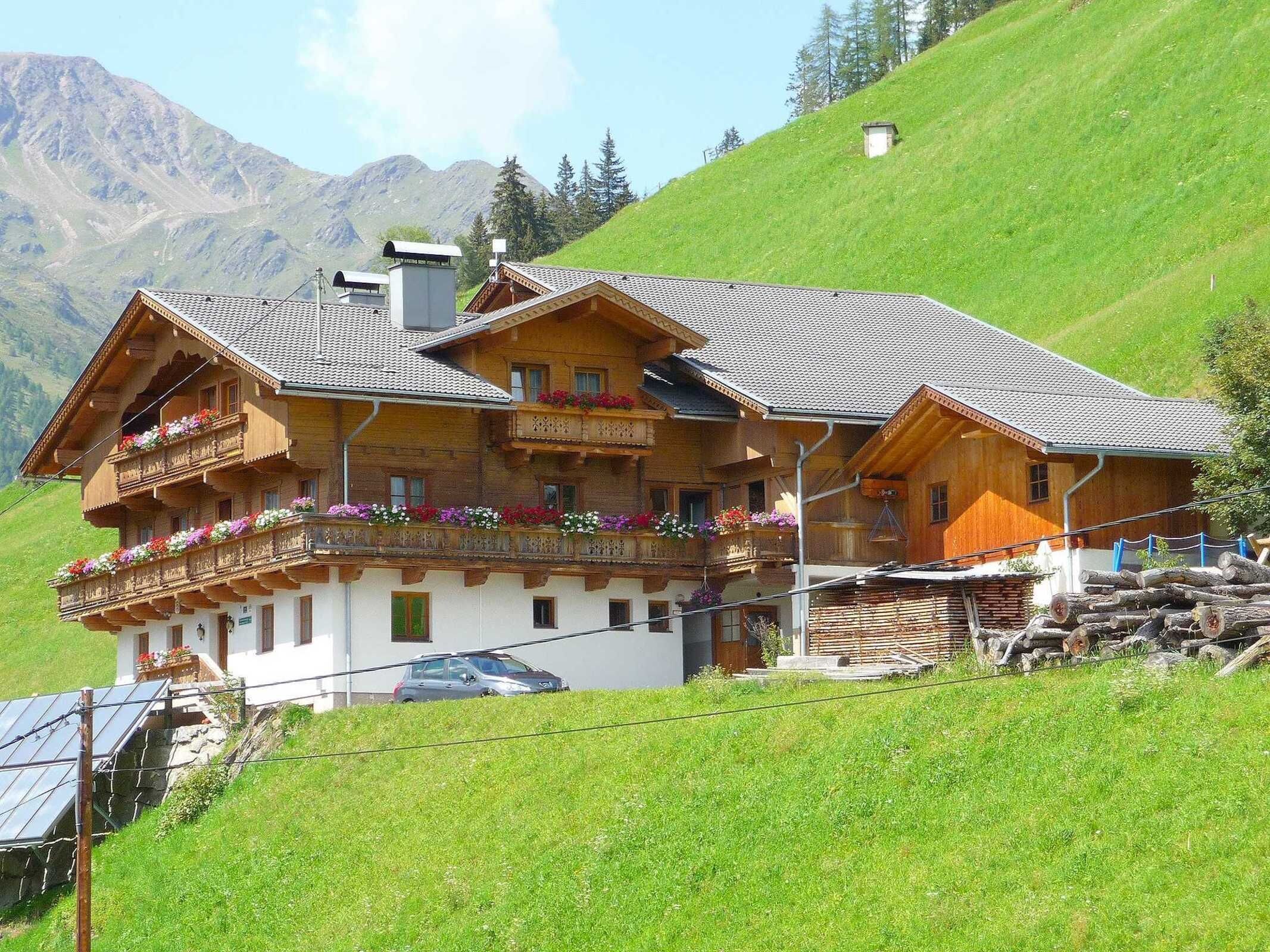 A wooden chalet with balconies, a car parked in front, and a mountainous backdrop.