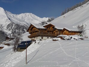 Eine Holzchalet mit einem Balkon, umgeben von schneebedeckten Bergen.