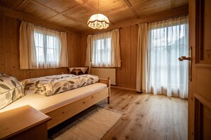 A wooden room with a bed, a nightstand, a window with curtains, and a chandelier. - Apartment House Gutwenger surrounded by the Dolomites (Innervillgraten)