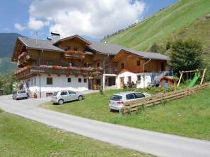 A two-story wooden house with a balcony, a car parked in front, and a playground with a slide. - Apartment House Gutwenger surrounded by the Dolomites (Innervillgraten)
