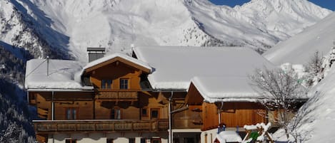 A wooden chalet with a balcony, surrounded by snow-covered mountains.