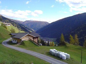 A rural house with a sloped roof, a paved road, and hay bales in the foreground. - Apartment House Gutwenger surrounded by the Dolomites (Innervillgraten)