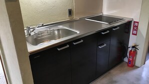 Une cuisine de taille réduite, dotée d’un évier en acier inoxydable, d’une cuisinière encastrée et d’armoires noires.