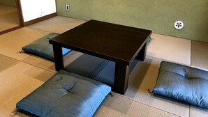 Une pièce avec un sol recouvert de tatamis, une table en bois foncé et des coussins assortis.