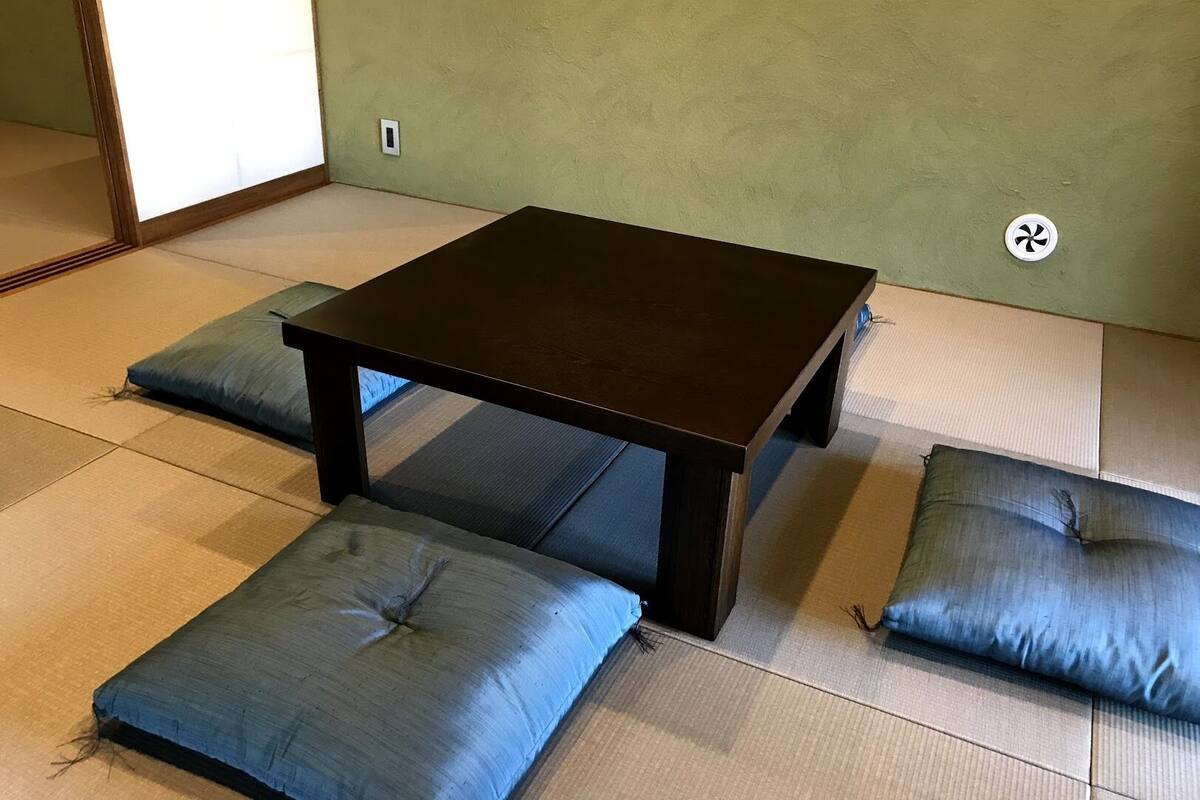 Um espaço com esteiras de tatame, uma mesa de madeira escura e almofadas combinando.