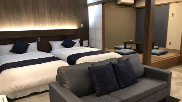 Une chambre d’hôtel avec deux lits, un canapé gris et une tête de lit en bois.