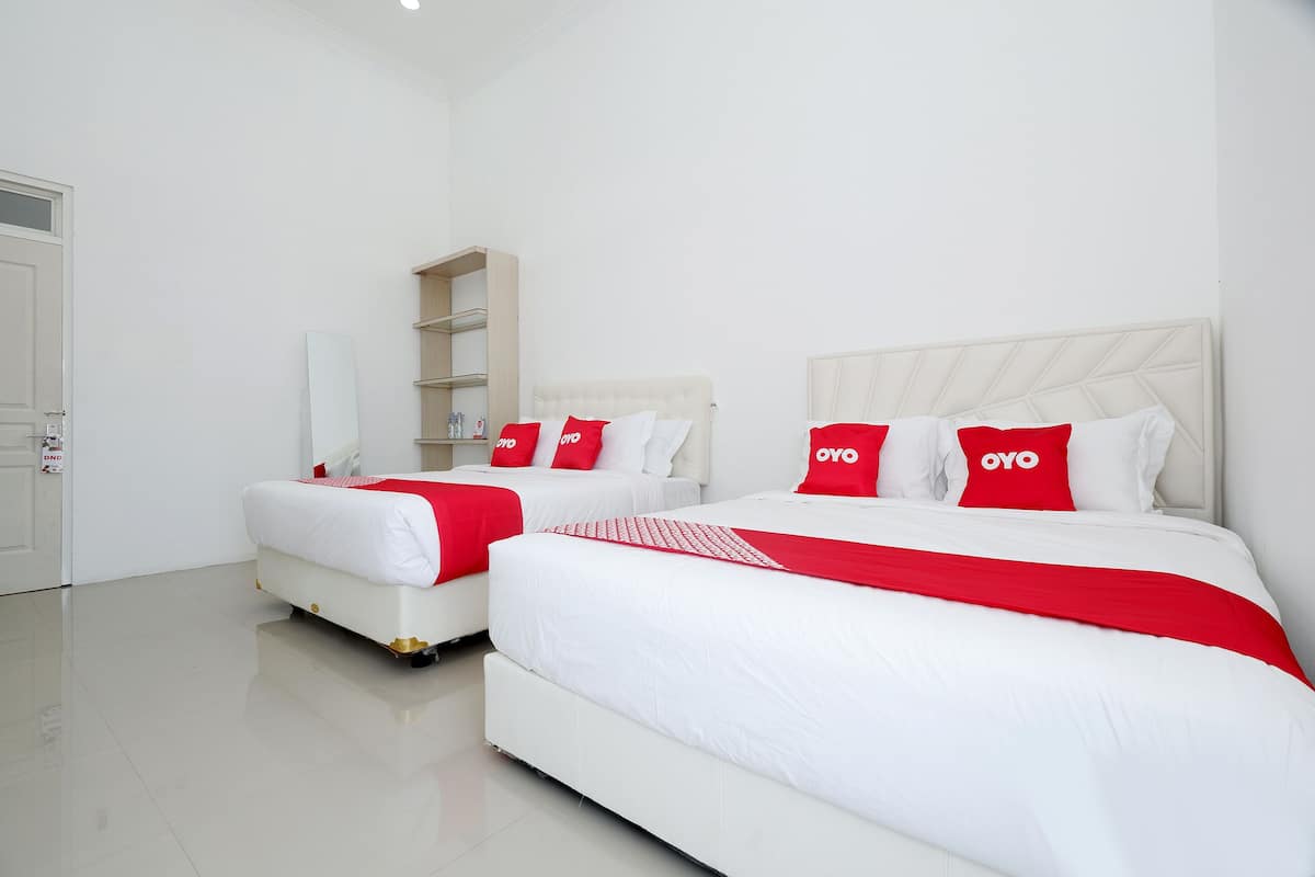 Habitación de hotel con dos camas, cada una con ropa de cama blanca y detalles rojos, un armario blanco y un espejo.