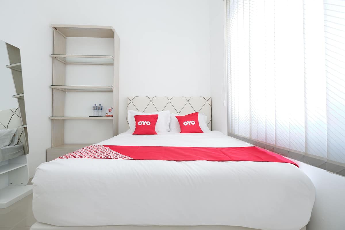 Habitación de hotel ordenada con una cama grande, una mesita de noche y una estantería empotrada.