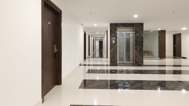 A modern hotel corridor with a marble floor, wooden doors, and a glass elevator. - Collection O 30002 Bhel Hyderabad (Sangareddi)
