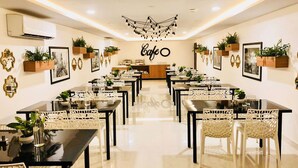A modern cafe with black tables and white chairs, decorated with plants and framed pictures. - Collection O 30002 Bhel Hyderabad (Sangareddi)