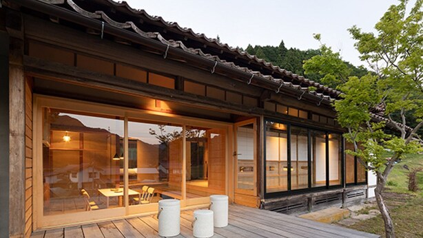 En traditionel japansk bygning med træterrasse, store skydedøre af glas og udsigt over det omkringliggende landskab.