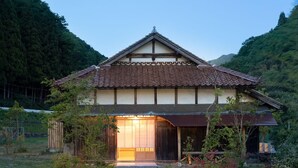 Et traditionelt japansk hus med et fliset tag, træbjælker og en stor åben indgang.