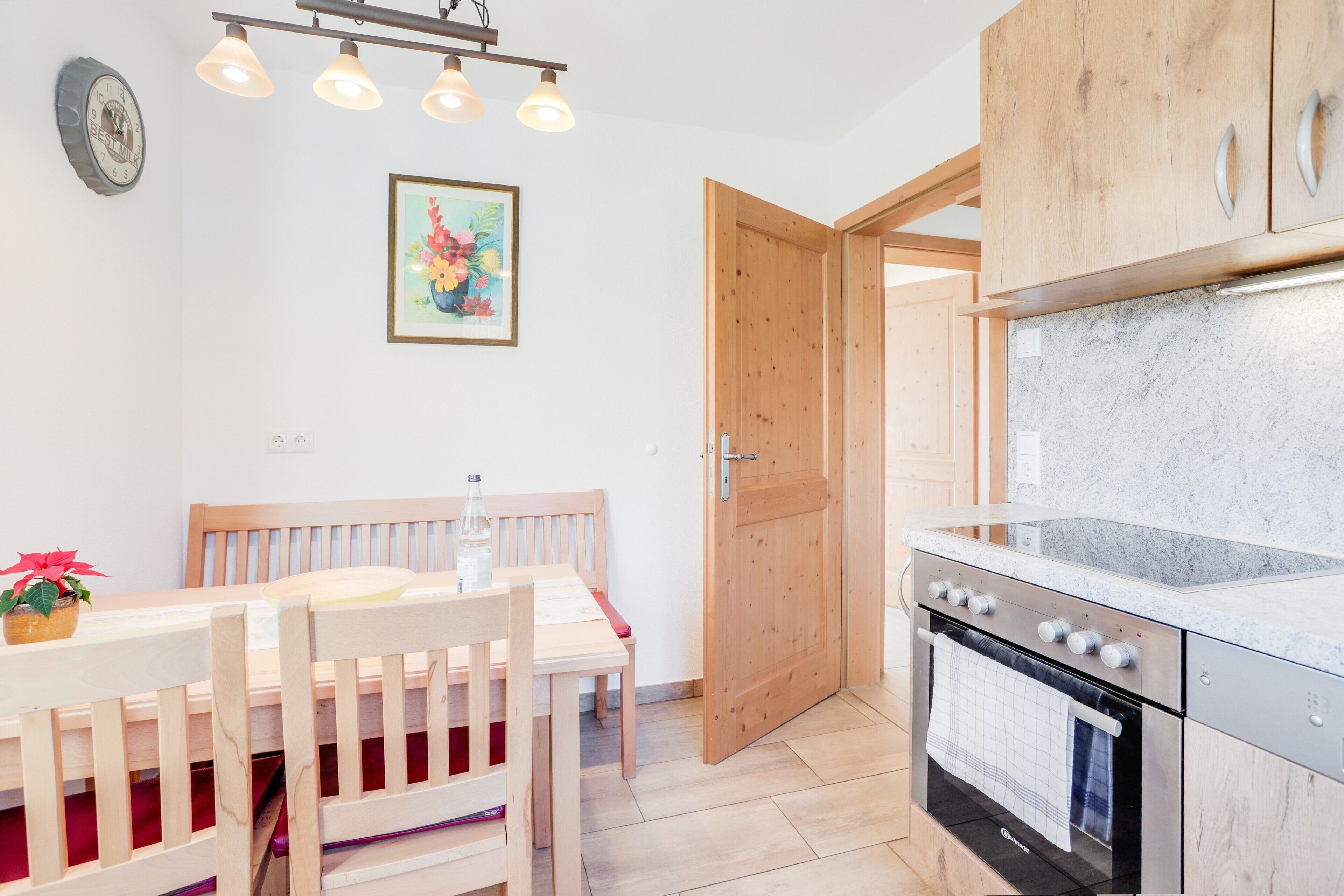 Een keuken met houten kastjes, een oven van roestvrij staal, en een eethoek met een houten tafel en stoelen.