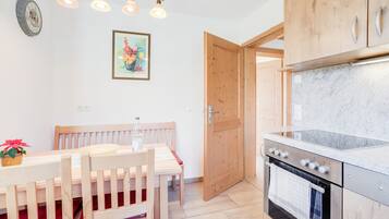 Een keuken met houten kastjes, een oven van roestvrij staal, en een eethoek met een houten tafel en stoelen.