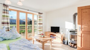 A bedroom with a bed, a TV, a wooden table, a fireplace, and a view of the outdoors. - Cosy Apartment "Bergblick" with Garden, Terrace & Wi-Fi; Parking Available (Bad Heilbrunn)