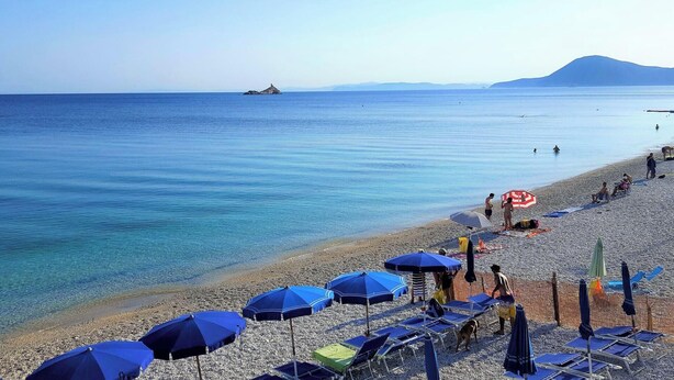 A beach with clear blue water, a rocky shoreline, and several umbrellas and lounge chairs. - Villa Bel Panorama - a beautiful house with an amazing sea view (Portoferraio)