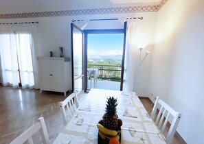 A dining area with a table set for two, a pineapple centerpiece, and a view of a cityscape through a glass door.