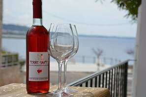 A bottle of Terre Sante wine and an empty glass on a balcony with a view of the sea.