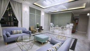 Una sala de estar moderna con un sofá, un reposapiés y una mesa de centro de vidrio. Hay una zona de comedor con sillas blancas y una mesa.
