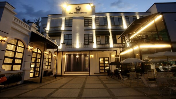 El exterior del Hotel Stanton, con una entrada bien iluminada, un área de asientos al aire libre y una vista clara del nombre del hotel en la fachada.