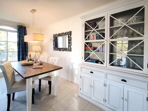 A dining area with a wooden table, white chairs, a chandelier, a mirror, and a white cabinet with glass doors. - Haus Meeresblick FeWo Strandlöper C 2.02 Ref. 134796 - FeWo Strandlöper C 2.02 (Baabe)