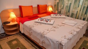 Un lit bien fait, recouvert d’une couvre-lit à motifs floraux, avec deux oreillers et une lampe de chevet posée sur une table de nuit en bois.
