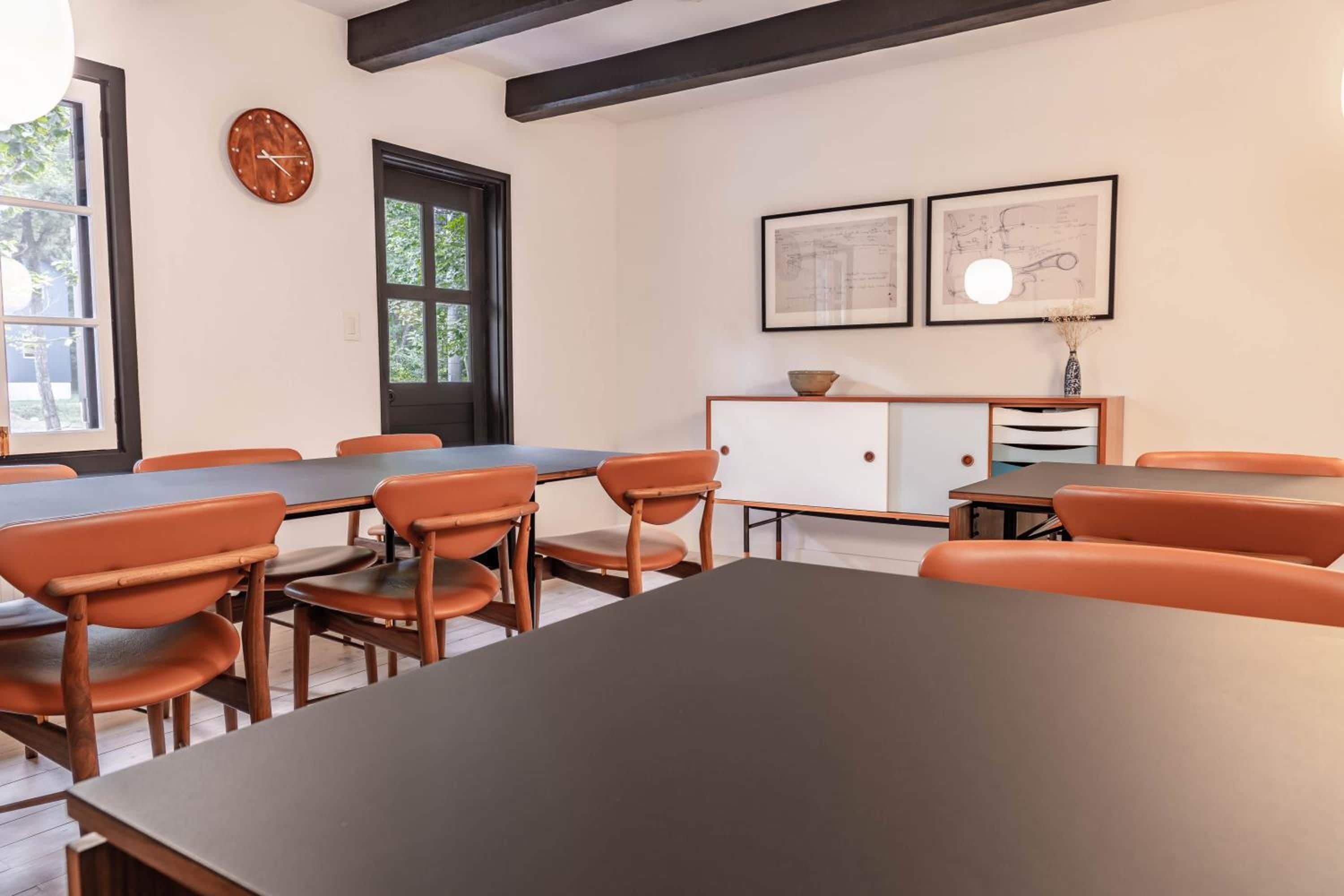 Ein Konferenzraum mit einem langen Tisch, orangefarbenen Stühlen, einer Holzkabine und gerahmten architektonischen Plänen an der Wand.