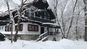 A traditional chalet with a steep roof, wooden balcony, and red shutters. It is surrounded by snow-covered trees and a snow-covered ground. - House of Finn Juhl Hotel Hakuba (Hakuba)