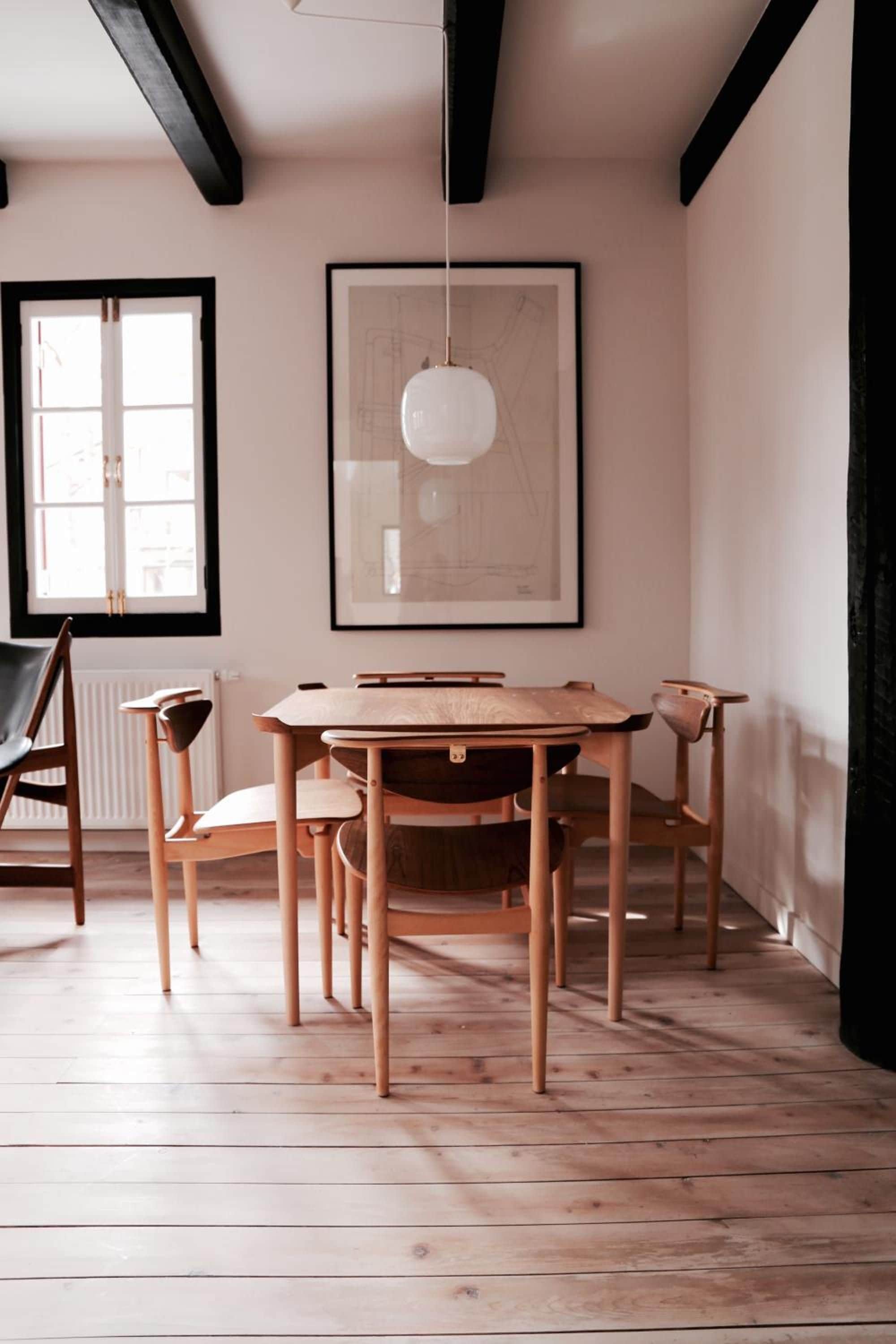 A dining area with a wooden table and chairs, a pendant light, and a large framed architectural drawing on the wall.