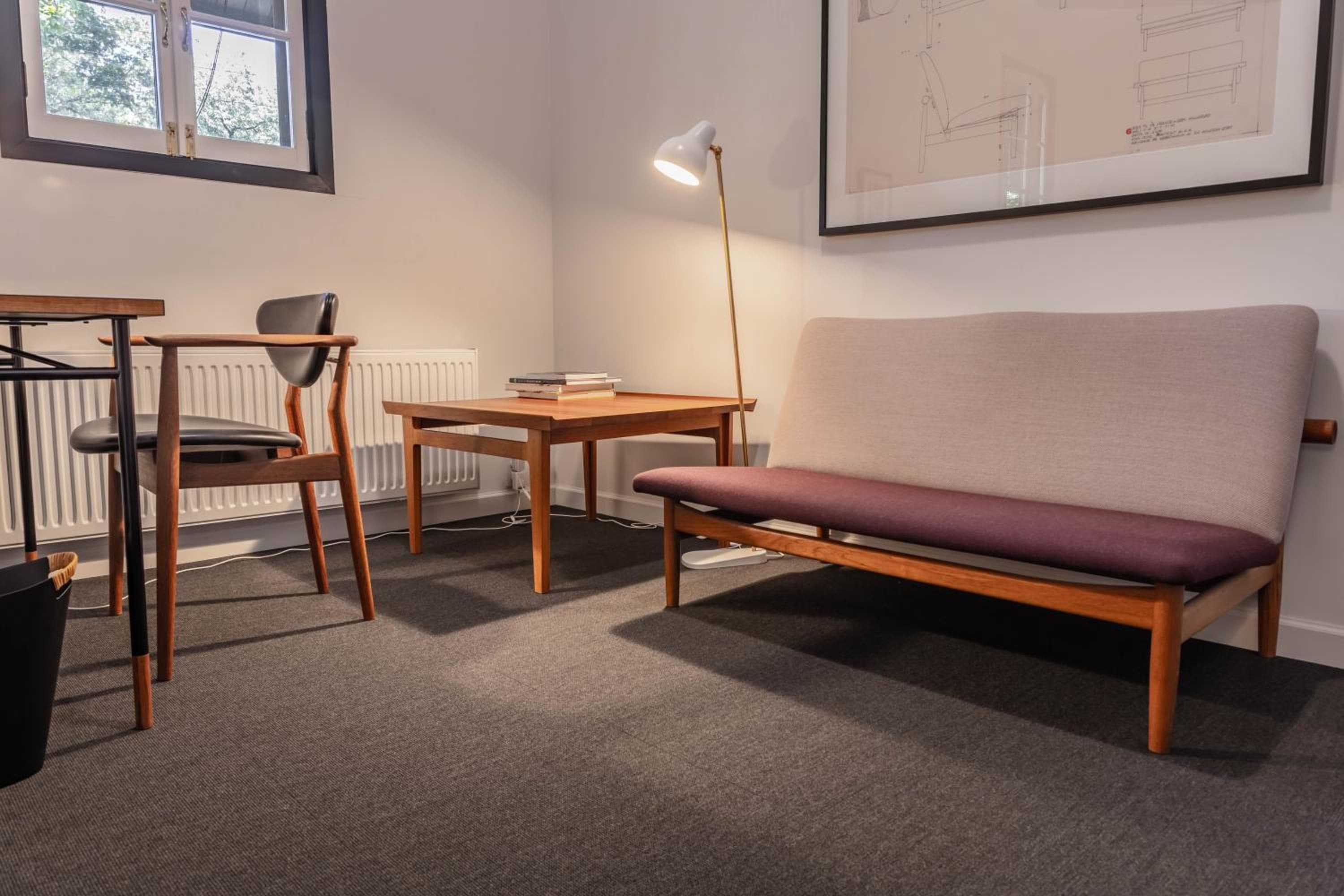 Une pièce comprenant un bureau en bois, une chaise, un canapé et un lampadaire.