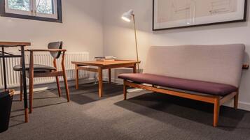 Une pièce comprenant un bureau en bois, une chaise, un canapé et un lampadaire.