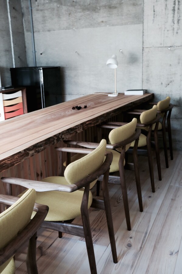 A long wooden table with matching chairs, a white desk lamp, and a black television in a room with concrete walls and wooden flooring.