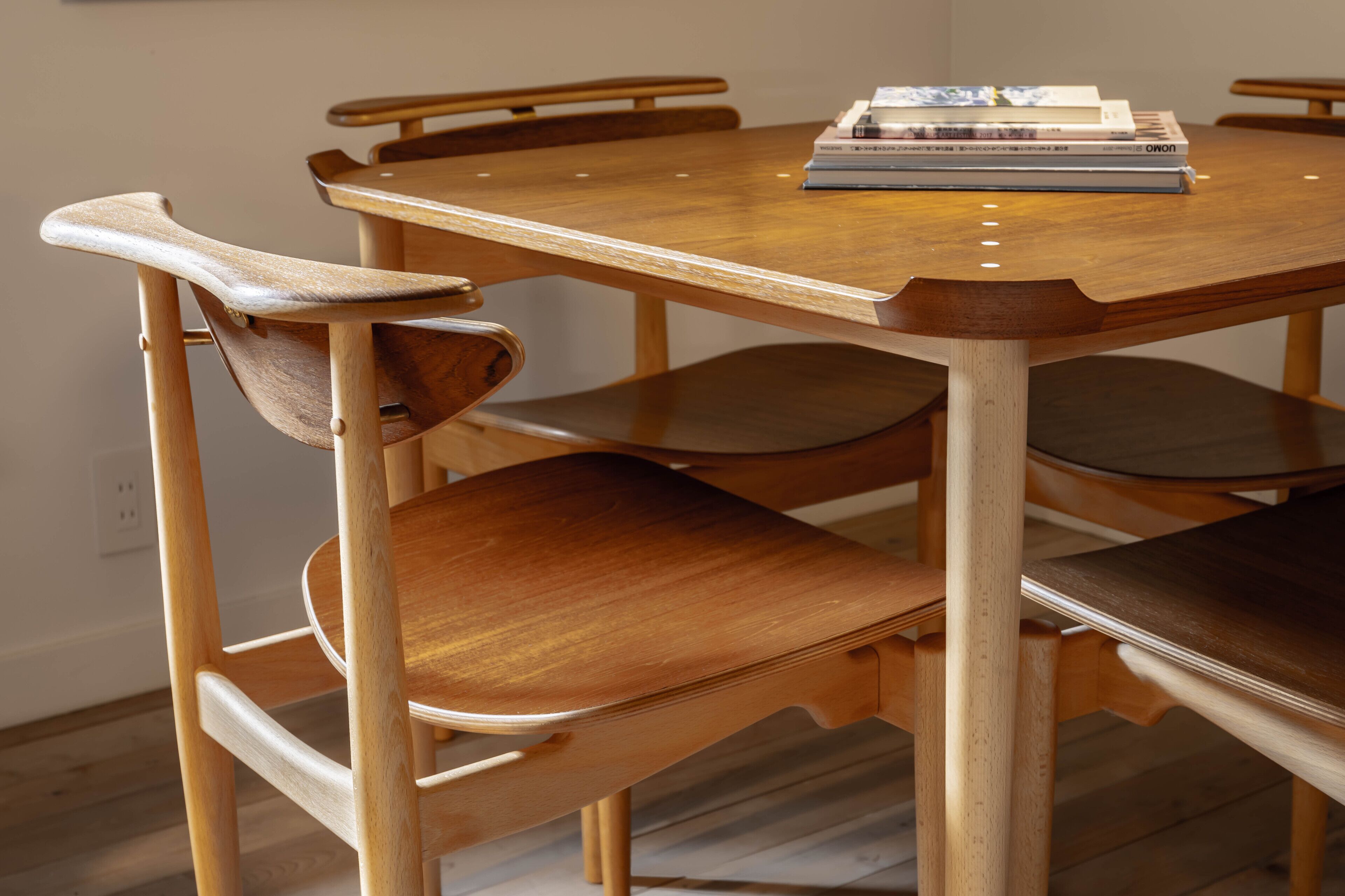 A wooden dining table with six chairs, a stack of books, and a power outlet on the wall.