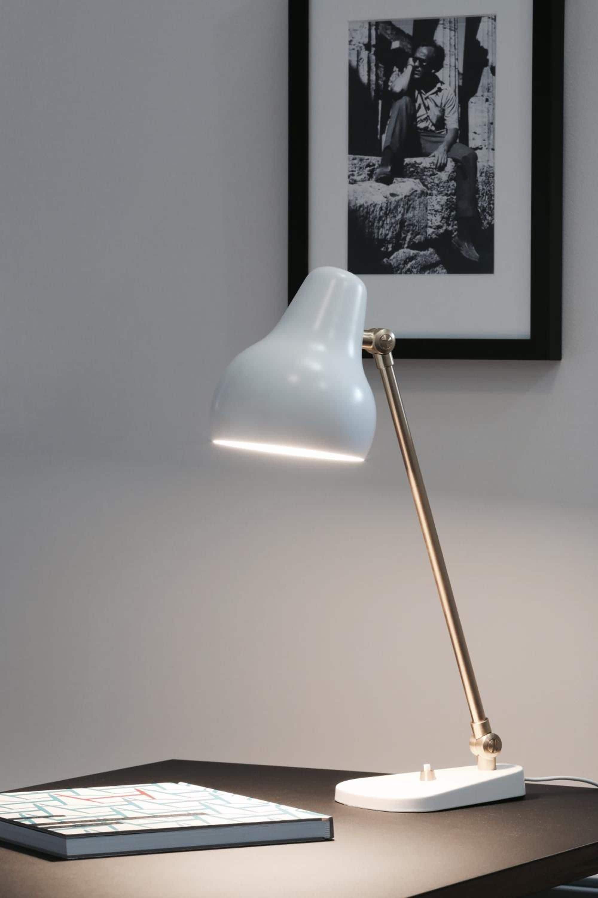 A desk with a white desk lamp and a framed picture on the wall.