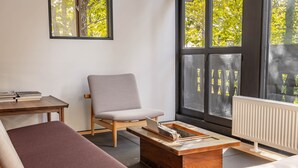 A modern living room with a sofa, armchair, coffee table, and a view of trees through large windows. - House of Finn Juhl Hotel Hakuba (Hakuba)
