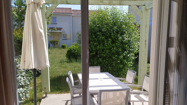 Un patio con mesa y sillas, un espacio de estar cubierto y vista a una casa y follaje.